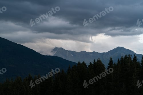 Preview: High-angle shot of Mittersill mountains with tree silhouettes and low clouds sitting on the peak