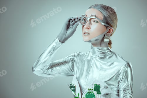 Preview: futuristic silver robot adjusting eye prosthesis and looking away isolated on grey, future