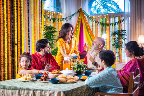 Preview: Portrait of happy Indian family in traditional outfit celebrating Diwali at home eating food