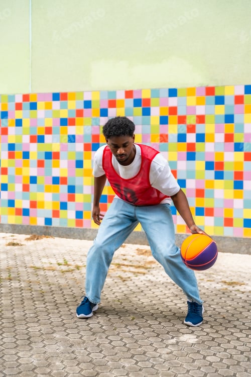 Preview: Young man dribbling basketball in front of colorful wall