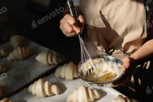 Preview: Female baker smears raw croissants with a brush in the yolk, the cooking process.