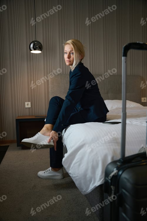Preview: Businesswoman is taking sports shoes off tired legs in hotel room