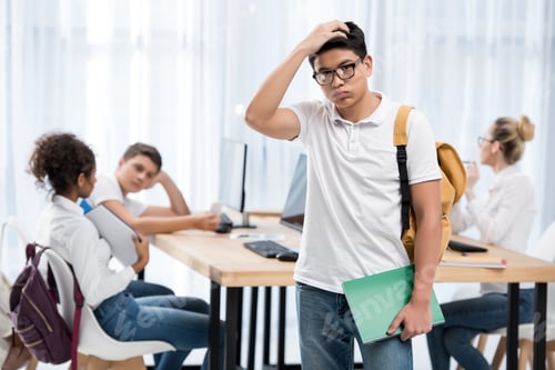 Preview: young pensive asian student boy in classroom with friends