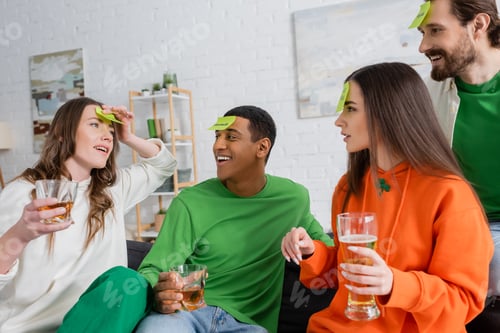 Preview: interracial friends with sticky notes on foreheads playing guess who game on Saint Patrick Day