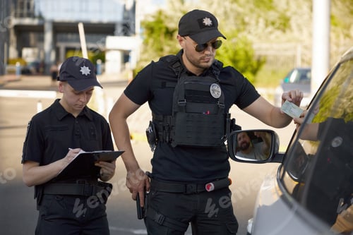 Preview: Patrolman and patrolwoman team writing traffic ticket for parking violation