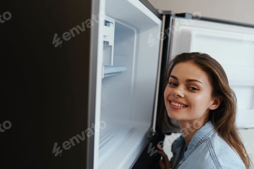 Preview: Young woman smiling while looking into an open refrigerator, showing joy and healthy lifestyle