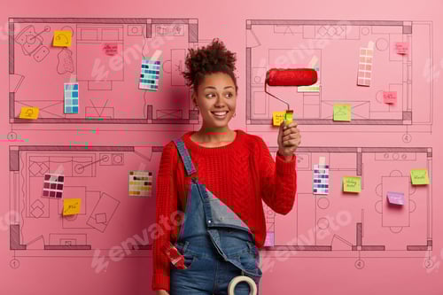 Preview: Glad smiling Afro American decorator holds paint roller, busy doing repairing according to design pr