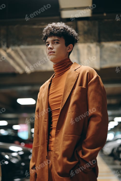 Preview: Stylish young man in orange outfit standing confidently in a modern parking garage