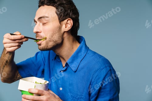 Preview: Pleased handsome guy smiling while eating salad takeaway