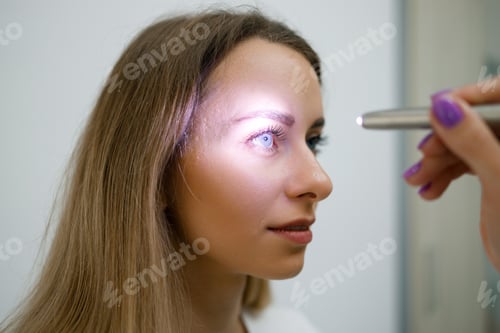 Preview: Close up view of doctor testing reflexes of the eye of young woman using a flashlight