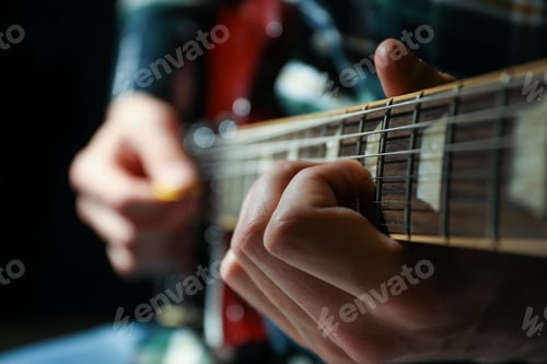 Preview: Man playing on electric guitar against dark background, closeup