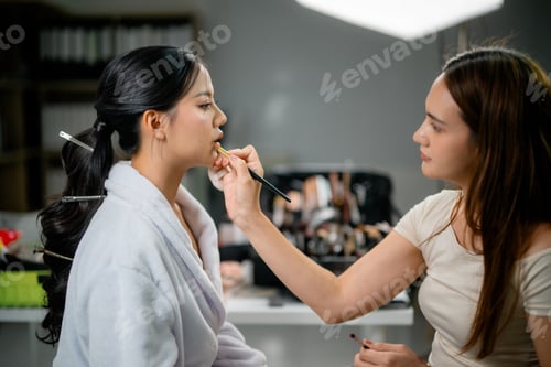 Preview: Makeup artist applying lipstick on model lips in beauty salon