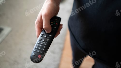 Preview: a person holds the tv remote watching series at home