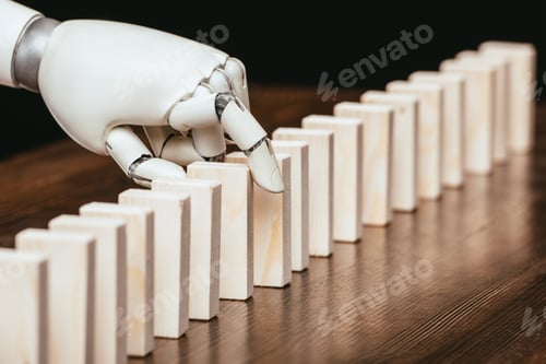 Preview: selective focus of robotic hand picking wooden brick from row of blocks on desk