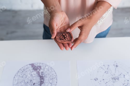 Preview: partial view of astrologer holding clay rune near blurred celestial charts