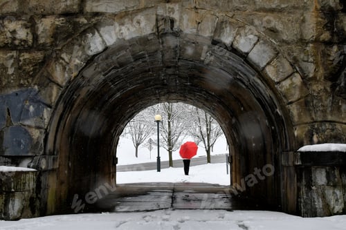 Preview: Woman with red umbrella walking in snow in city park through a stone tunnel, Winter storm, weather