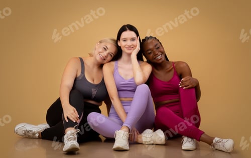 Preview: Multi ethnic female friends in sportswear posing in studio, sitting on floor