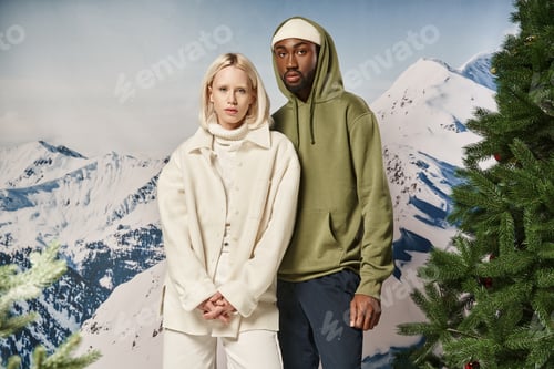 Preview: stylish diverse couple in warm trendy jackets posing and looking at camera, winter concept