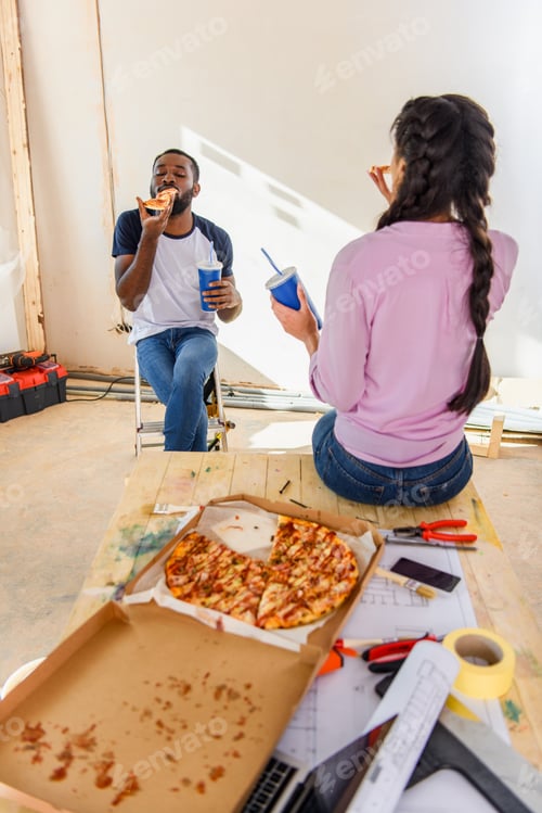 Preview: african american couple having lunch with pizza and soda during renovation at home