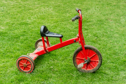 Preview: Red used tricycle on lush green grass. Close-up.