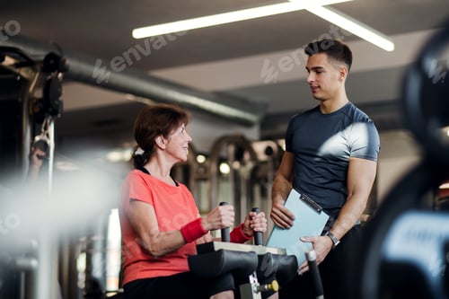 Preview: A female senior with a young trainer doing strength workout exercise in gym.