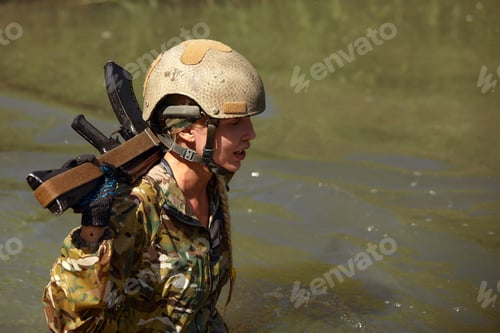 Preview: Portrait of fit military female holding weapon rifle in hands in river, posing alone. Confident