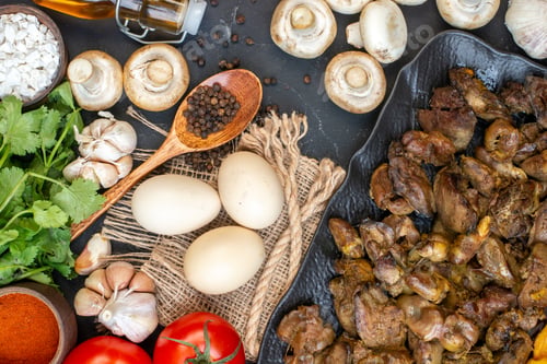 Preview: top view tasty kebab on platter eggs garlic mushrooms black pepper in wooden spoon tomatoes on dark