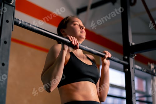 Preview: in the gym a coach girl in black leggings and a top is doing pull-ups on the horizontal bar