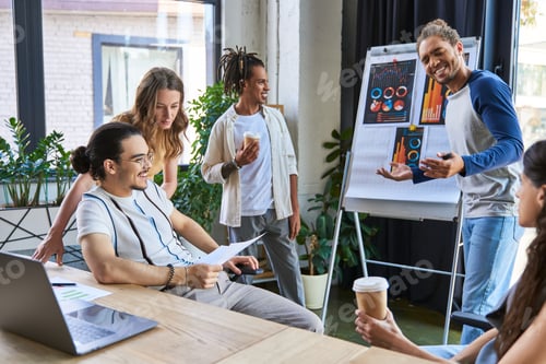 Preview: joyful african american man talking near flip chart during meeting with multiethnic team in office