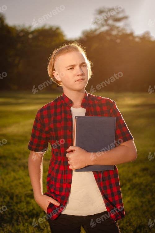 Preview: serious teenager holding notebook or textbook and looking into the distance in sunny day