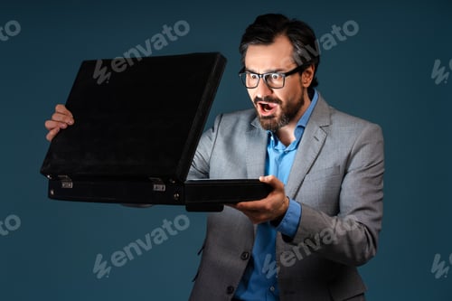 Preview: Surprised man in glasses opening the briefcase and looking at the light inside in the dark