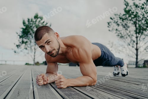 Preview: Motivational bearded man stands in plank pose, trains muscles and has strong body