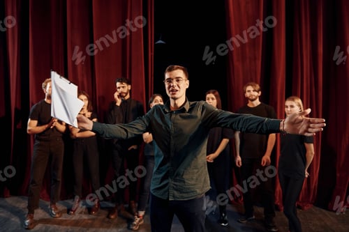 Preview: Man is practicing his role. Group of actors in dark colored clothes on rehearsal in the theater