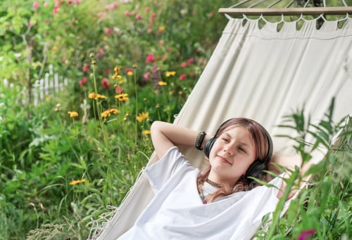 Preview: Teenage girl relaxing in hammock listening to music in garden