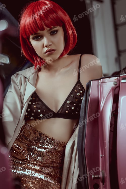 Preview: beautiful young woman in fashionable trench coat looking at camera while sitting in retro car