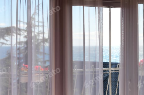 Preview: Window and curtains with view of sea in hotel room.