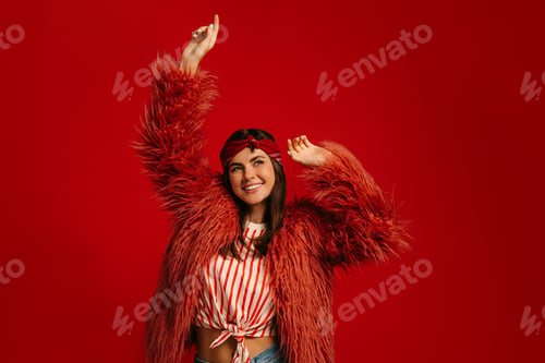 Preview: Joyful young hipster woman in fluffy coat dancing against red background