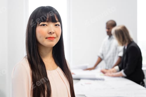 Preview: Professional woman in an office setting with colleagues discussing in the background.