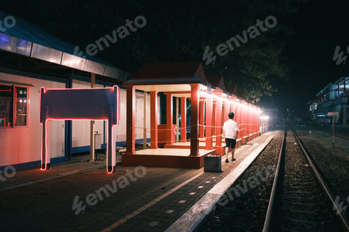 Preview: Empty night train station with man walking, illuminated shelter and track