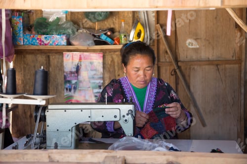 Preview: A focused artisan sewing with diligence in her wooden workshop