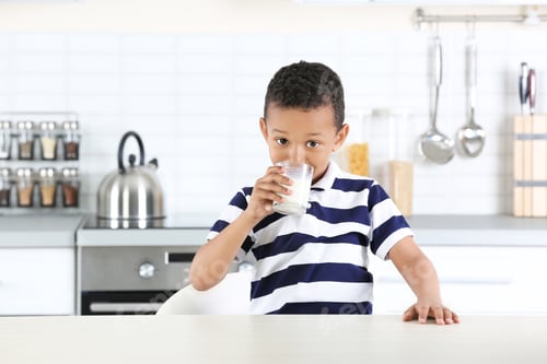 Preview: Adorable African-American boy with glass of milk in kitchen