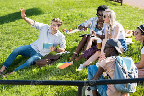 Preview: cheerful multiethnic students resting together on green grass in park