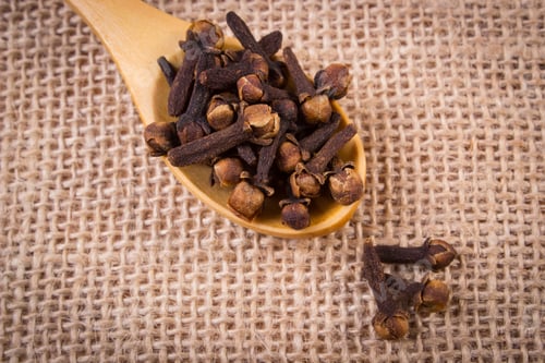 Preview: Heap of cloves with wooden spoon on jute canvas, seasoning for cooking