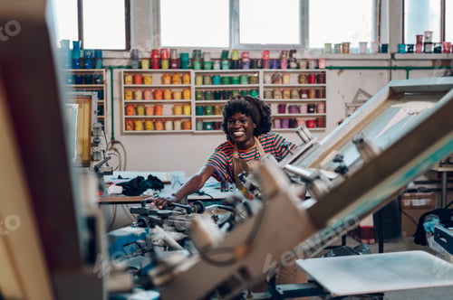 Preview: Happy diverse graphic technologist adjusting silkscreen printing press