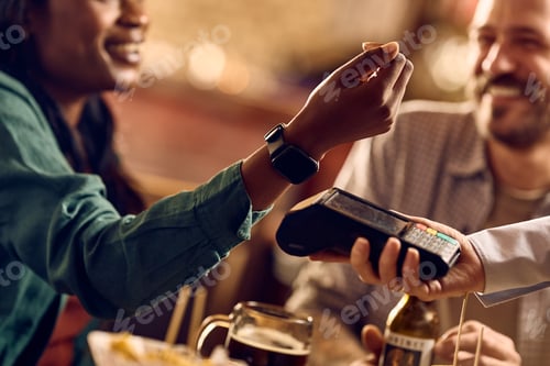 Preview: Close up of black woman paying contactless with smart watch in a bar.