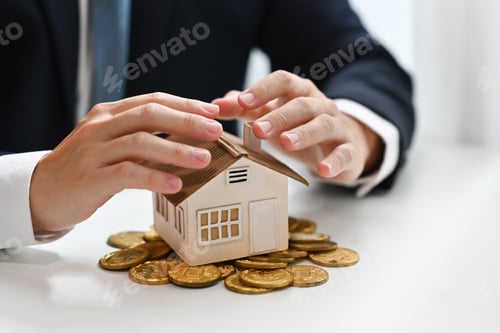 Preview: Businessman hands protecting house model and pile of gold coins.