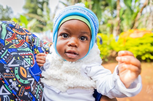 Preview: Cute healthy little African baby boy carried in an adult's arm looking at the camera