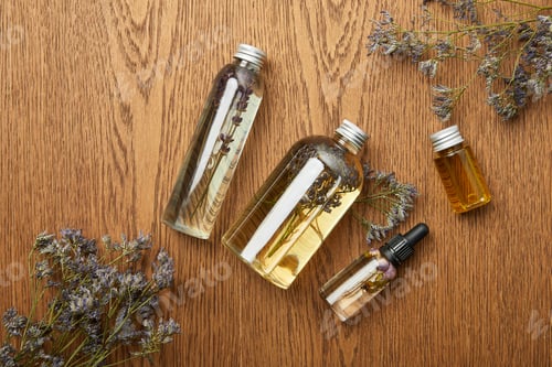 Preview: top view of transparent bottles with organic beauty products near dried herbs on wooden background