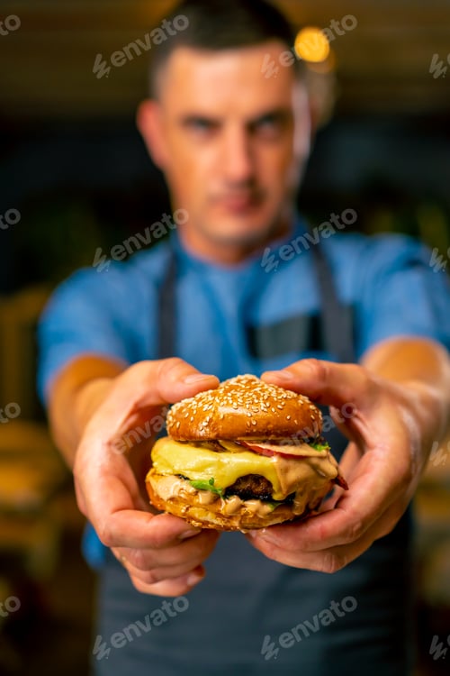 Preview: The chef of an Italian restaurant in uniform shows the burger he cooked in his professional kitchen