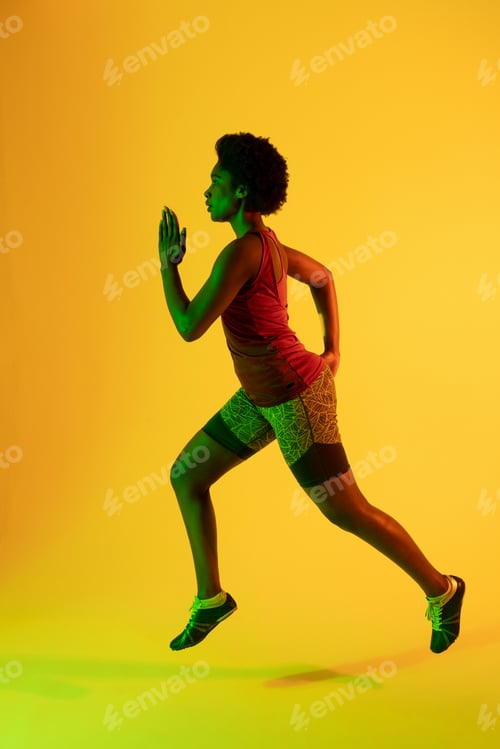 Preview: Vertical image of african american female athlete running in yellow lighting
